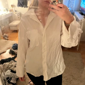 Vit långärmad skjorta - Säljer en klassisk vit skjorta i bomull. Den har en normal passform och långa ärmar, perfekt för både vardag och fest. Skjortan har en enkel bröstficka och knappar framtill. Den är i bra skick men något skrynklig, vilket lätt fixas med strykjärn. Perfekt för vår och sommar!