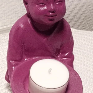 Romantiskt röd i glitter  ljushållare i form av en buffhs - Säljer en unik ljushållare i form av en knäböjande buddha i en härlig graffiti sprayfärg. Perfekt för värmeljus och ger en mysig stämning i rummet. Den är gjord av ett glittrigt material som fångar ljuset fint. Perfekt som dekoration eller present!