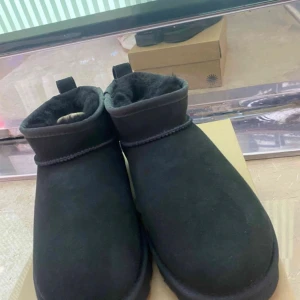 Svarta boots från UGG - Säljer ett par svarta UGG-boots i mycket bra skick. De är gjorda av mocka och har en mysig pälsfodring inuti. Perfekta för kalla dagar när du vill hålla fötterna varma och bekväma. De har en enkel design med en liten flärp baktill för lättare påtagning.