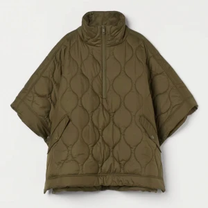 Olivgrön quiltad poncho - Säljer en olivgrön quiltad jacka med korta ärmar, dragkedja framtill och knappar på sidorna. Perfekt för höstpromenader, den har en loose passform och hög krage för extra värme. Jackan har praktiska fickor med knappar. Superfin att styla med en stickad tröja under! Några skinnfläckar på kragen som säkert går bort i tvätten. Våga pruta!!