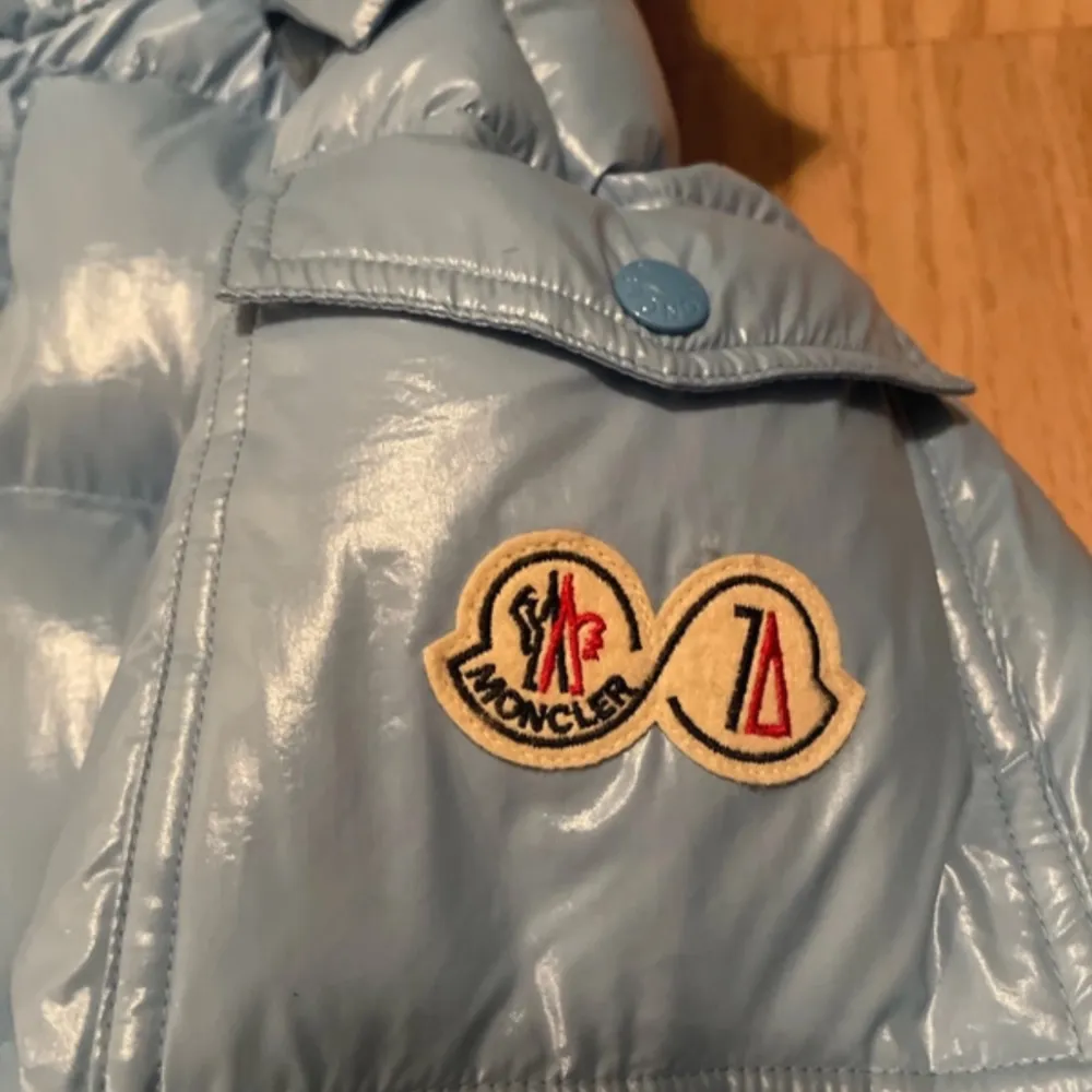 Säljer en snygg ljusblå pufferjacka från Moncler. Jackan har en quiltad design med en mysig huva och knappar framtill. Den är perfekt för kalla dagar och har en cool Moncler-logga på ärmen. Dragkedjan är robust och det finns en rolig serietidning på insidan. Perfekt för vintern! ❄️. Jackor.