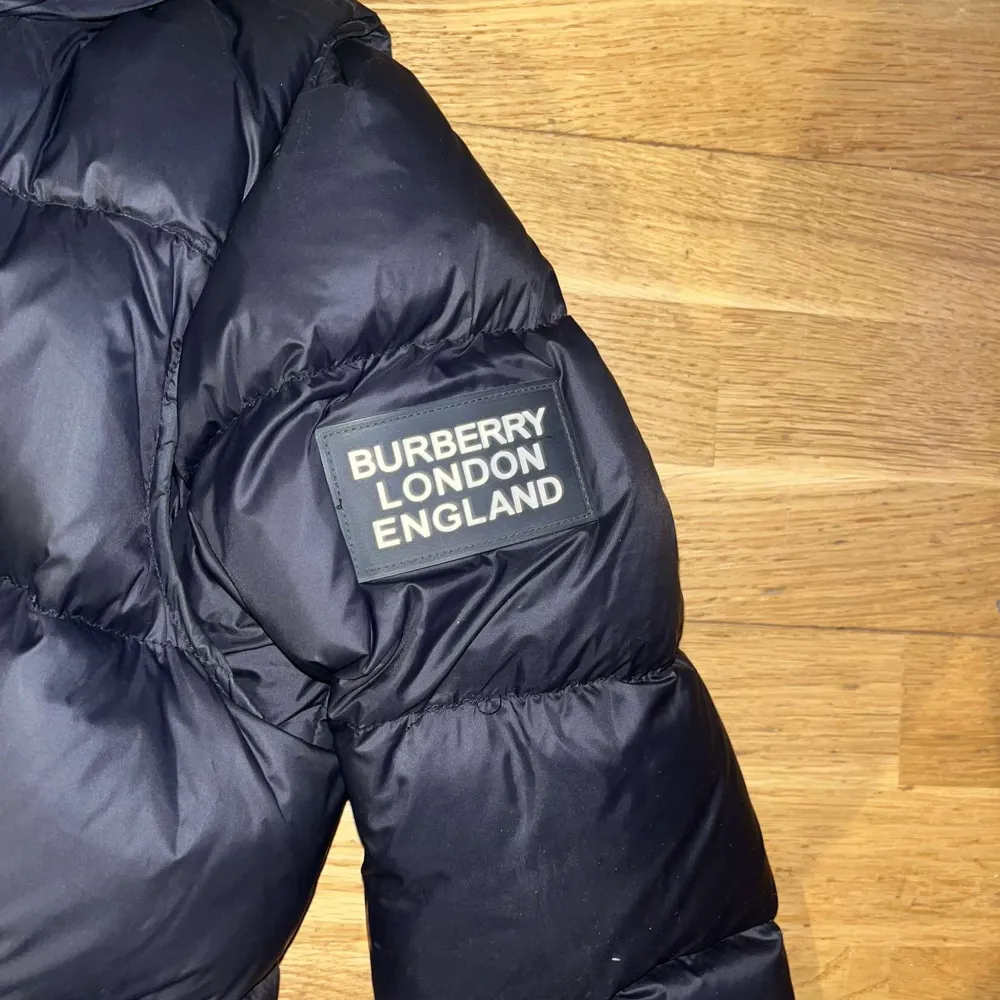 Säljer en snygg svart pufferjacka från Burberry London. Jackan håller dig varm inför vintern och har en stilig burberry rutat mönster i luvan. Storlek S/XS. Jackor.