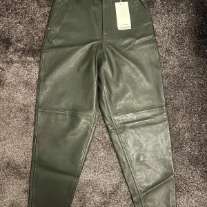 Mörkgröna skinnbyxor från Five Units - Säljer ett par snygga mörkgröna skinnbyxor från Five Units i modellen Alba. Byxorna är i storlek 26. De är tillverkade i äkta läder och har en normal passform. Passar både till vardags och fest!