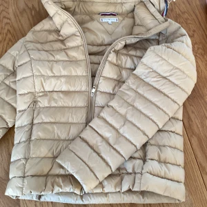 Beige jacka från Tommy Hilfiger - Säljer en snygg beige jacka från Tommy Hilfiger i storlek XS. Jackan har en dragkedja och är perfekt för höst och vår. Den är i mycket bra skick och har en klassisk design med en mysig huva. Perfekt för att hålla värmen när det är kyligt ute!