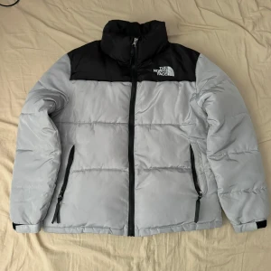 Grå och svart jacka från North Face - Säljer en snygg och varm dunjacka från The North Face i grått och svart. Jackan har en dragkedja framtill och två praktiska fickor med dragkedjor. Perfekt för kalla vinterdagar! 🖤Jackan passar som M