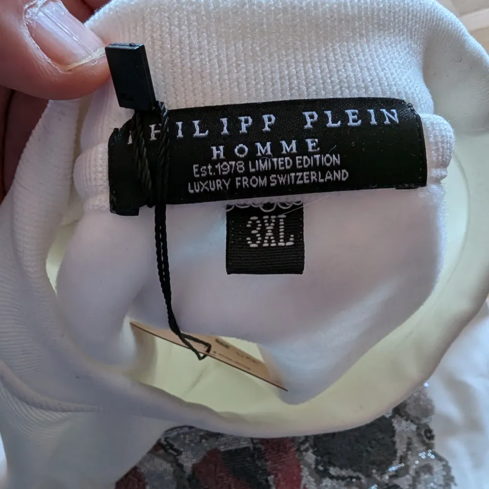 Säljer en cool vit sweatshirt från Philipp Plein med ett stort dödskalletryck i grått och rött på framsidan med kristaller. Tröjan är i nytt skick och har en liten passform, passar mer som en L eller XL. Perfekt för en avslappnad stil med en edgy twist. Passar bra till både jeans och joggers!. Tröjor & Koftor.