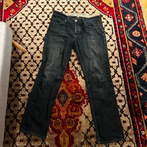 Mörkblå jeans - Säljer ett par mörkblå jeans i bra skick. De har en klassisk straight passform med fem fickor och knappgylf. Perfekta för vardagsbruk och kan enkelt matchas med olika stilar. Passar bra till både höst och vår.