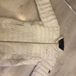 Vit pufferjacka från Sailracing  - Säljer en snygg vit pufferjacka från Sailracing . Jackan har en dragkedja framtill och är quiltad för extra värme. Perfekt för kyliga höst- och vinterdagar. Den är i mycket bra skick och har en stilren design med ett märke på ärmen. Priset går att diskuteras, byten fungerar också 🙌