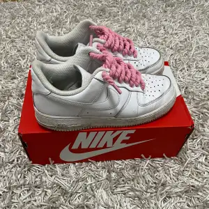 Säljer ett par klassiska Nike Air Force i vitt med coola rosa snören. Skorna är i bra skick och har en stilren design med perforerade detaljer på tån för extra ventilation. Perfekta för både vardag och fest! Kommer i originalkartong.