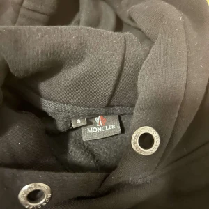 Svart hoodie från Moncler - Säljer en snygg svart hoodie från Moncler i storlek S. Den har en klassisk design med Moncler-loggan broderad på bröstet och en patch på ärmen. Perfekt för höst och vinter, med en skön passform och långa ärmar. Huvan har dragsko för justering. Perfekt för en stilren och bekväm look! Pris kan diskuteras!