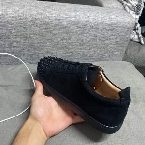 Säljer ett par svarta sneakers i mocka från Christian Louboutin. Skorna har coola nitar på tån och den ikoniska röda sulan. Perfekta för att ge din outfit en edgy touch. De är i perfekt skick, strlk 44 oanvänd