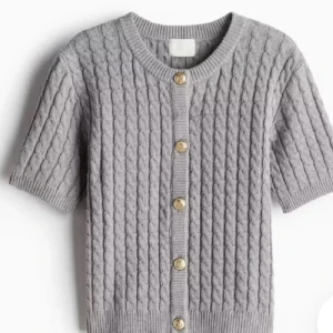 Super eftertraktad grå stickad kofta med korta ärmar - Säljer en superfin grå stickad kofta med korta ärmar och snygga guldknappar. Perfekt för lager-på-lager under hösten eller våren. Den har en klassisk kabelstickad design som ger en tidlös look. Passar både till vardags och lite finare tillfällen. 🧶✨