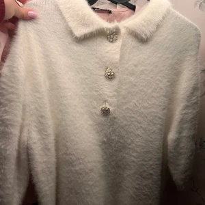 Vit fluffig kofta med pärlknappar - Superfin vit tröja med kortare armar i fluffigt material med tre glittrande pärlknappar framtill. 🤍 Stl S/M 