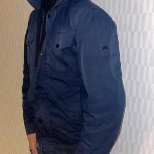 J.lindberg Jacka  - Säljer en snygg mörkblå jacka från J.Lindeberg. Den har en stilren design med knappar och dragkedja framtill. Den är i toppen skick som nytt. Färgen är mörkblå och jackan är tjock och kan vara väldigt bra att ha nu till vintern. Storleken är M men passar även S, modellen är 1,82. Mvh 101 store🙌🏼