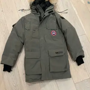 Säljer en grön parkajacka från Canada Goose med pälsdetaljer på huvan. Jackan är perfekt för kalla vinterdagar och har en quiltad insida för extra värme. Den har långa ärmar och flera praktiska fickor. Notera att ärmmuddarna är något slitna. Perfekt för vinterns äventyr! ❄️