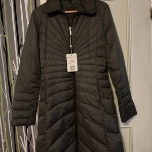 Gröngrå dunjacka från Moncler - Säljer en elegant svart dunjacka från Moncler i mycket bra skick. Jackan har en stilren design med långa ärmar och dragkedja framtill. Perfekt för kalla vinterdagar och håller dig varm och snygg. Passar både till vardags och festliga tillfällen.