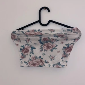Blommig tubtopp - Söt blommig tubtopp i vitt med rosa och gröna blommor. Perfekt för sommardagar eller en festlig kväll. Toppen är ärmlös och har en tight passform som framhäver figuren. Materialet är mjukt och stretchigt för extra komfort.
