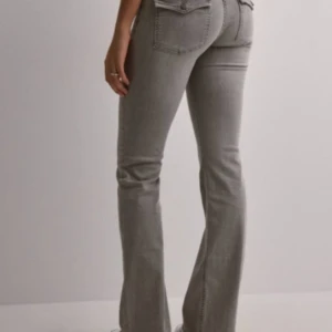 Grå jeans från Nelly - Säljer ett par snygga grå jeans från Nelly. Lågmidjade & bootcut. De är i bra skick och har en klassisk femficksdesign med knappar och dragkedja framtill. Nypris: 699 kr