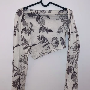 Vit blommig offshoulder topp - Säljer en superfin vit offshoulder topp med svart blommönster. Den har långa ärmar och en asymmetrisk design som ger en unik look. Perfekt för vår och sommar! 🌸