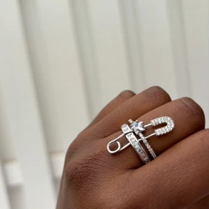 Exklusiv Cuffring med säkerhetsnål detalj - En elegant och unik cuffring i rostfritt stål, dekorerad med gnistrande kubisk zirkonia och en trendig säkerhetsnålsdetalj.