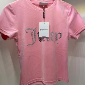 Rosa velour t-shirt från Juicy Couture - Säljer en superfin rosa t-shirt i velour från Juicy Couture. Den har ett glittrigt 'Juicy'-tryck på framsidan. Kortärmad och i storlek M. Helt ny med prislapp kvar.