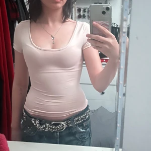 Ljusrosa tight topp - Säljer en ljusrosa tight topp med korta ärmar. Den är enkel och stilren, perfekt för vardagsbruk eller att klä upp med accessoarer. Toppen är i ett mjukt och stretchigt material som sitter bekvämt på kroppen.