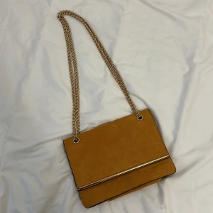 Gul axelväska från New Look - Säljer en superfin gul axelväska från New Look. Den har en snygg kedjerem och en stilren design med en metallisk detalj på framsidan. Perfekt för både vardag och fest! 💛