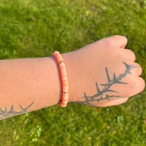 Orange armband med gulddetaljer - Säljer ett snyggt armband i en härlig orange färg med små gulddetaljer. Perfekt för att liva upp vilken outfit som helst! Armbandet är elastiskt och passar de flesta handleder. Perfekt accessoar för sommarens alla äventyr! 🌞