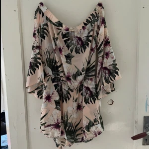 Blommig kortklänning från Amisu - Säljer en superfin blommig kortklänning från Amisu i storlek EU 34. Klänningen har en ljus bas med gröna och vinröda blommor och blad. Den är perfekt för sommaren med sin lösa passform och korta ärmar. Perfekt för en dag på stranden eller en sommarfest!