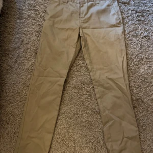 Beige chinos från Dickies - Säljer ett par snygga beige chinos från Dickies. De har en slim fit passform som sitter riktigt bra och ger en stilren look. Perfekta för både vardag och lite mer uppklädda tillfällen. Materialet känns slitstarkt och av hög kvalitet. Kan mötas upp i 