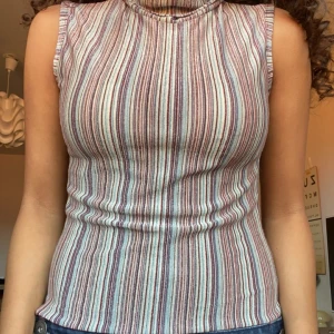 Randig ärmlös topp - Säljer en superfin ärmlös topp med randigt mönster i olika färger som röd, vit och beige. Den har en hög krage och är gjord i ett stretchigt material som sitter tight och bekvämt. Perfekt för både vardag och fest! Den har även glitter trådar som gör den så fin ❤️