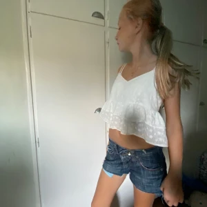 Vit blommig linne topp - Säljer en superfin vit linne topp med blommigt mönster. Toppen är ärmlös och har en luftig, croppad passform med volangdetaljer. Perfekt för sommardagar och kan stylas med jeansshorts för en avslappnad look.