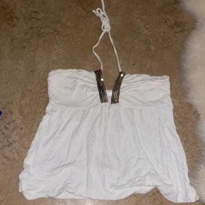 Topp - Vit guldigt linne med knytning i nacken. Vintage från 90-talet, själv aldrig använt. Alla paljetter är kvar, finns ett litet hål men går lätt att laga. Inbyggd bygel mellan bröstet så den sätter sig väldigt fint på kroppen. Sitter bra som S/M.