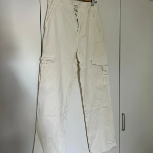 Vita cargobyxor från Pull&Bear - Säljer ett par snygga vita cargobyxor från Pull&Bear. De har en avslappnad passform med praktiska fickor på sidorna. Perfekta för en casual look eller att klä upp. Byxorna är i bra skick och passar S-M beroende på hur man vill att de ska sitta 