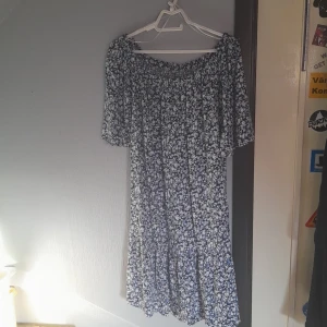 Blommig klänning - Säljer denna klänning då den inte kommit till användning. Klänningen är blommig och har färgen blå, svart och vitt.