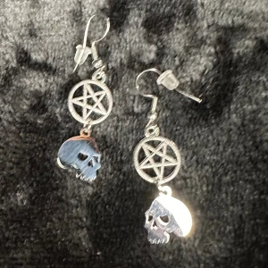 Unika nya örhängen med pentagram och dödskallar Nya Ockult Satanic Unika Metal Rock Punk Biker Bundlerabatt  - Säljer ett par riktigt grymma silverfärgade örhängen med pentagram och dödskallar av rostfritt stål. Längd drygt 4 cm, bredd 1,3 cm. Hypoallergena krokar. Gummistoppar medföljer.  Nytillverkat och egendesignat av mig @bybasen. Unika och uppseendeväckande.