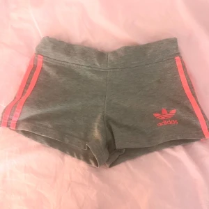 Adidas shorts i neonrosa och grå - Fina adidas shorts i neonrosa och grå! Har en pytte liten fläck som går att ta bort💕