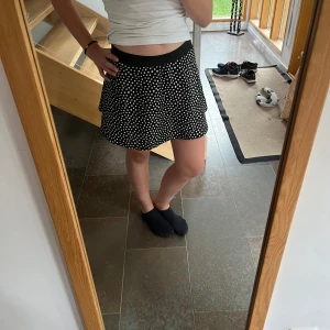 Svart prickig kjol från Kids - Säljer en superfin svart kjol med vita prickar från märket Kids by Lindex. Kjolen är kort och har en elastisk midja som gör den bekväm att bära. Perfekt för både vardag och fest! 🖤