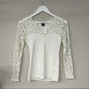 Vit spetsblus från H&M - Säljer en elegant vit blus från H&M med spetsdetaljer på ärmarna och överdelen. Blusen har långa ärmar och en v-ringad design som ger en stilren look. Perfekt för att klä upp en outfit med en touch av romantik.