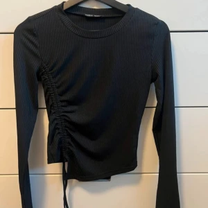 Svart ribbad topp med knyt - Snygg svart ribbad topp från Zara med långa ärmar och knytning på sidan. Perfekt för en stilren look.
