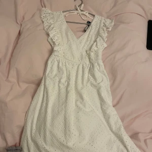Vit klänning / Studentklänning  - Säljer en söt vit klänning från Vero Moda med volangdetaljer och v-ringning. Klänningen har ett fint broderat mönster och knytband i ryggen. Perfekt för sommarens alla tillfällen! 🌸