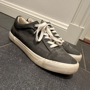 Svart/gråa sneakers med vita snören - Snygga svart/grå sneakers med vita snören och sula. Perfekta för en avslappnad stil. De har en klassisk design med låg profil och rund tå. Storlek 39 men sitter som en 38!!