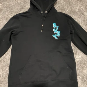 Risky Hoodie - Säljer en svart hoodie med en cool design av blå fjärilar på framsidan. Tröjan har en klassisk känguruficka och justerbar huva med snören. Perfekt för en avslappnad stil.