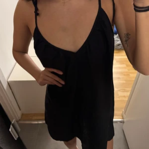 Svart klänning från H&M - Snygg svart klänning från H&M med smala axelband och v-ringning. Perfekt för en stilren look. Klänningen har en luftig passform och är tillverkad i ett lätt material.