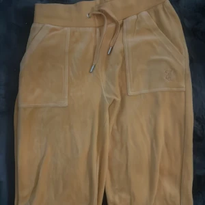 Orangea mjukisbyxor från Juicy Couture - Snygga orangea mjukisbyxor från Juicy Couture med snörning i midjan och stora fickor fram. Baktill finns fickor med knappar. Perfekta för en avslappnad stil. Jackan är i XS och byxorna är i S, nya men var inte nöjd med färgen eftersom färgen inte passade mig!