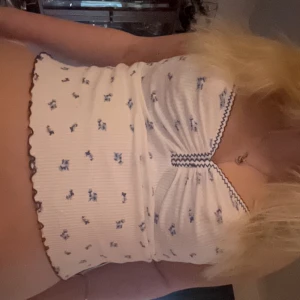 Vit ribbad linnetopp med blå blommor - Söt vit ribbad linnetopp från BDG med små blå blommor och dekorativa kanter. Toppen har smala axelband och en knuten detalj framtill💕