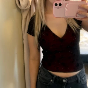 Vinröd topp med spetsdetaljer - Snygg vinröd topp med blommigt mönster och spetsdetaljer vid halsringningen. Knappt använd!