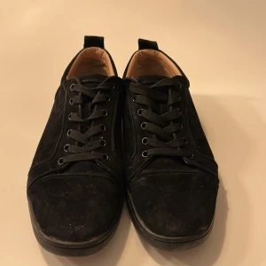 Svarta sneakers med röd sula - Snygga svarta sneakers i mocka med en iögonfallande röd sula. Skorna har klassisk snörning och en bekväm innersula i beige. Perfekta för en stilren look. Ända problemet är att det har gått sönder lite av sulan på vänster sko.