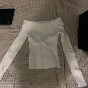 Vit offshoulder tröja - Säljer en stilren vit offshoulder tröja med långa ärmar. Tröjan är ribbad och har en elegant design som passar perfekt för både vardag och speciella tillfällen. Perfekt för att hålla stilen året runt.