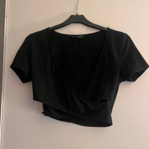 Svart omlottopp - Snygg svart omlottopp med korta ärmar. Perfekt för en stilren look. Toppen har en omlottdesign som ger en fin passform.